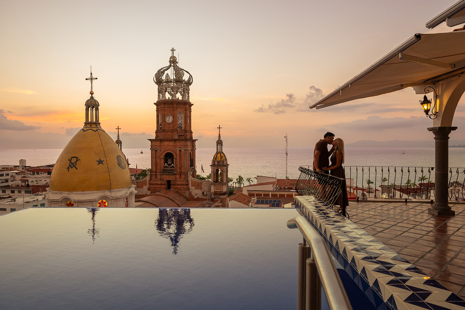 Couple kissing at sunset on a rooftop terrace facing the crowned cathedral and the bay of Puerto Vallarta